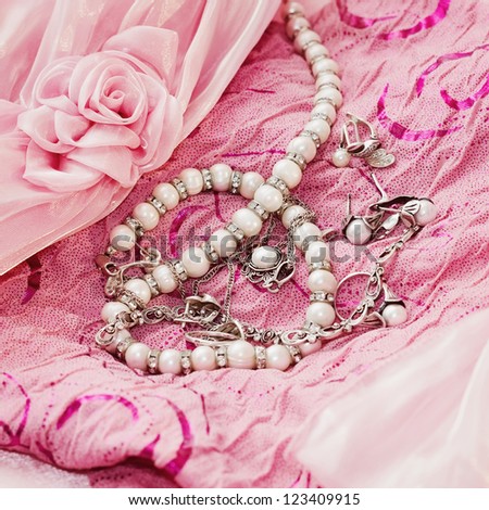 Different silver pear jewellery and closeup pearl on pink silk dress