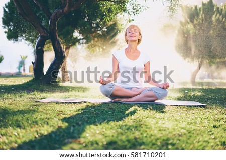Yoga at park. Senior woman in lotus pose sitting on green grass. Concept of calm and meditation.