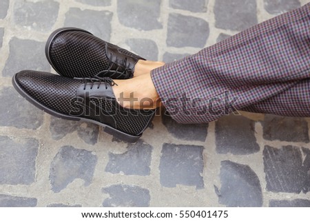 Man in checkered retro trousers in the city. Men's summer fashion, stylish men's shoes. Brown Perforated suede summer shoes with laces