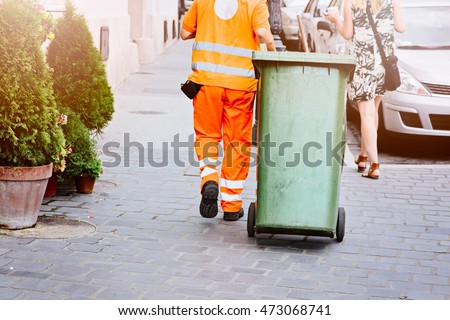 Worker of cleaning company in orange uniform with a green garbage bin
