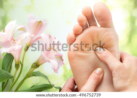 Macro cận cảnh massage chân bên cạnh hoa đầy màu sắc và nền màu xanh lá cây.