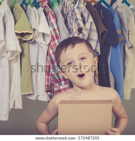 portrait of a little boy standing near a hanger with clothes at home at the day time