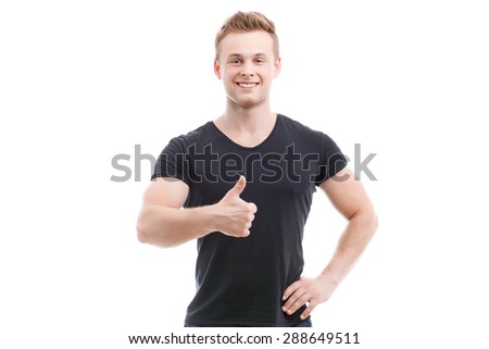 Half length portrait of a young handsome man wearing black t-shirt and blue shorts standing smiling and showing thumb up during training, isolated on white background
