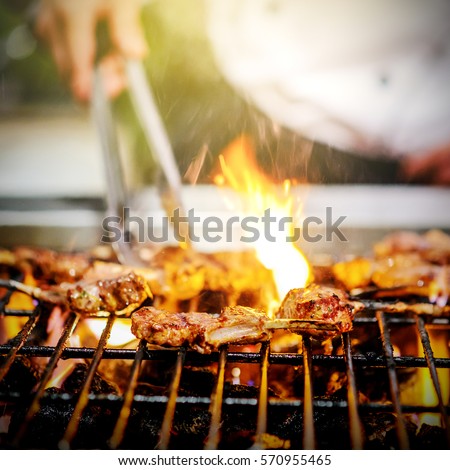 chef grilling lamb ribs on hot flame , barbecue cooking in evening and sunset