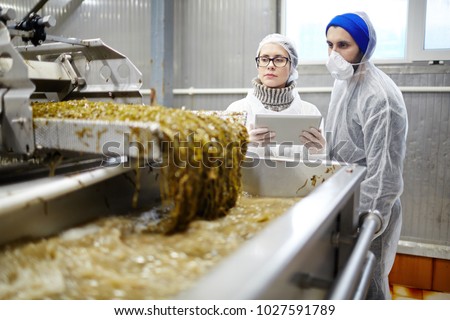 Control seafood factory staff in uniform standing by working industrial machine