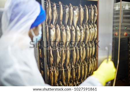 Staff in uniform pushing cart with several rows of smoked herrings