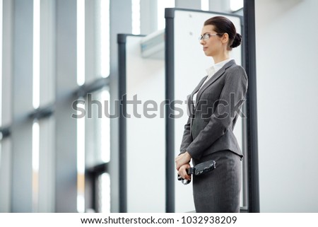 Young airport security with metal detector standing by gates on entrance