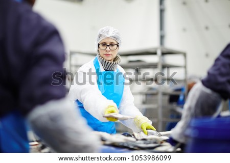 Young staff in uniform and her colleagues sorting frosted fish before processing