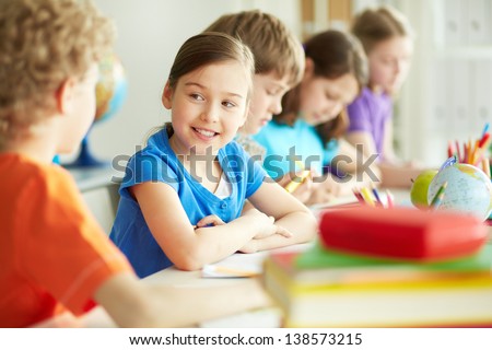 Portrait of happy diligent pupil looking at her classmate at lesson