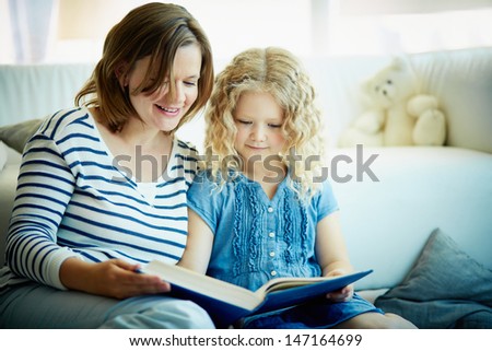 Portrait of cute girl and her mother reading a book at home