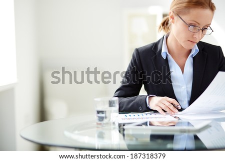Young businesswoman sitting at workplace and reading paper in office