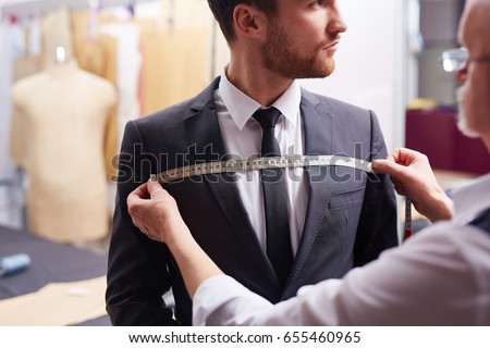 Portrait of tailor taking measurements of customer during model fitting