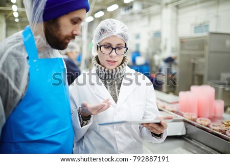 Colleagues from seafood processing plant discussing online data about canned food