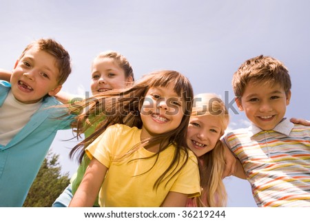 Portrait of happy children embracing each other and laughing with pretty girl in front