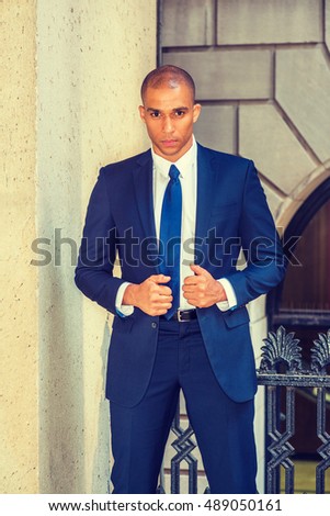 Portrait of Young European Businessman in New York. Wearing blue suit, white shirt, tie, Mixed Race French guy with shaved head stands outside office, seriously, tensely thinking. Filtered effect.