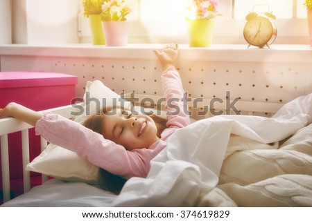 A nice child girl enjoys sunny morning. Good morning at home. Child girl wakes up from sleep.