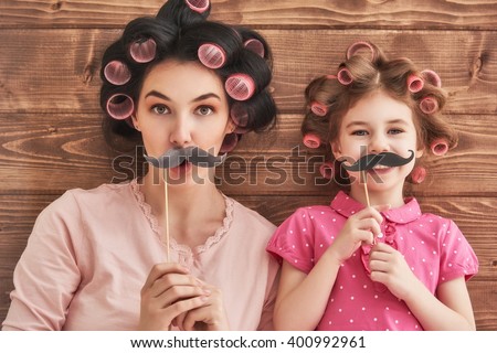 Funny family! Mother and her child daughter girl with a paper accessories. Beauty funny girl holding paper mustache on stick. Beautiful young woman holding paper mustache on stick.