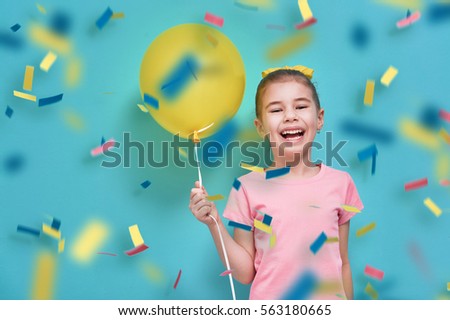 Funny child on a background of bright blue wall. Girl is having fun with balloons and confetti. Yellow, pink and turquoise colors.