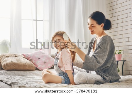 Happy loving family. Mother is combing her daughter's hair sitting on the bed in the room.