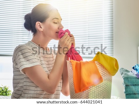 Beautiful young woman is smelling clean clothes and smiling while doing laundry at home.
