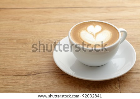 A cup of coffee with heart pattern in a white cup on wooden background - stock photo