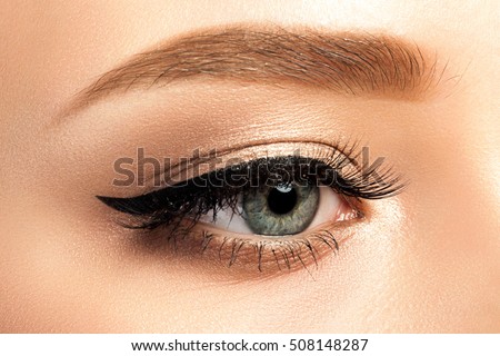 Close up view of gray woman eye with beautiful golden shades and black eyeliner makeup. Classic make up. Studio shot