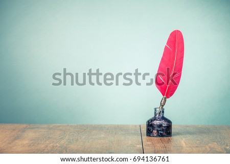 Vintage old red quill pen with inkwell on wooden table front gradient mint green wall background. Retro style filtered photo