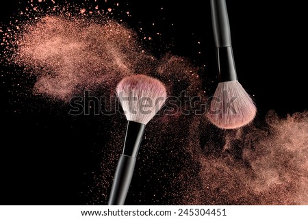 Make-up brush with pink powder explosion on black background