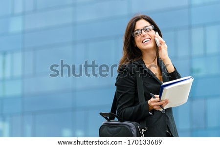 Successful businesswoman or entrepreneur taking notes and talking on cellphone while walking outdoor. City business woman working.