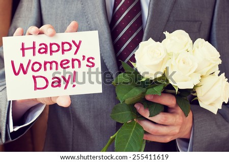Happy Women's Day! Man wearing a suit holding a greeting card and white roses