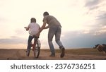 Small photo of dad teaches son to ride a bike. happy family kid dream concept. the boy sat on bicycle for the first time, his father teaches boy to ride a bicycle. dog lifestyle runs with family, fun family pastime