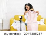 Beautiful african american girl vlogger or blogger sitting on sofa and live streaming for sale fashion clothing on social network. Her is influencer in social online. Social media marketing concept.