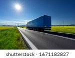Truck driving on the asphalt road between the yellow flowering rapeseed fields under radiant sun in the rural landscape