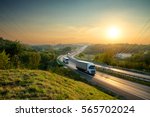 White trucks driving on the highway winding through forested landscape at sunset.