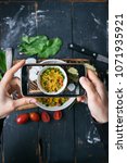 Small photo of Woman hands make smartphone photo of quinoa salad with vegetables - tomatoes, beans, greens - in white bowl on wooden board in dark style. Social networks phone photog. Vegan vegetarian healthy food