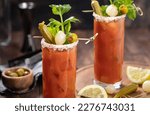 Small photo of Bloody mary cocktail garnished with celery, okra, onion, olive and salt rim on a dark wooden background