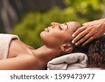 Small photo of Beautiful black woman getting face massage in luxury spa. African american girl relaxing in resort spa while getting head massage. Masseuse hands massaging black woman with closed eyes at resort spa.