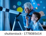 Small photo of Grandfather teaching grandson using telescope to see planets and galaxy. Child watching stars through a telescope at night with senior man. Grandpa and grandchild looking together at positive future.