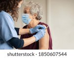 Small photo of General practitioner vaccinating old patient in clinic with copy space. Doctor giving injection to senior woman at hospital. Nurse holding syringe before make Covid-19 or coronavirus vaccine.