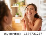 Small photo of Happy smiling beautiful girl cleaning skin face with cotton pad. Beauty natural woman looking in mirror while cleansing skin face and using cosmetic products for properly deep clean.