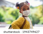 Small photo of Smiling cute little girl with school backpack and protective face mask ready for first day of school during covid pandemic. Black kid going back to school during coronavirus pandemic disease.