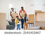 Small photo of African american family with two children carrying boxes in a new home. Cheerful mature mother and mid adult father holding boxes while entering new house with son and daughter with copy space.