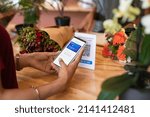 Small photo of Close up of woman hands scanning QR code with smartphone while paying florist. Woman paying cashless money using smartphone after buying flowers. Customer hand making payment through smart phone app.