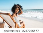 Portrait of happy african american woman sunbathing on wooden deck chair at tropical beach while looking at camera. Smiling black girl enjoying vacation at seaside with copy space. Woman relaxing.