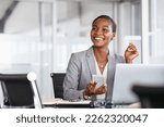 African black business woman using smartphone while working on laptop at office. Smiling mature african american businesswoman looking up while working on phone. Successful woman entrepreneur.