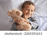 Small photo of Happy little boy hugging teddy bear with drip in hand smiling on hospital bed. Portrait of smiling child embracing teddy bear on gurney at private clinic. Cute kid with stuff toy lying on hospital bed