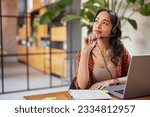 Small photo of Young latin business woman wearing headphones with microphone daydreaming while working on laptop. Thoughtful mixed race businesswoman take a break and thinking about new idea.