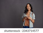 Small photo of Happy casual beautiful woman using smartphone isolated against grey background. Smiling hispanic young woman with backpack using mobile phone isolated against gray background with copy space.