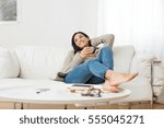 Young smiling woman sitting on sofa and looking up while drinking hot tea. Young brunette woman thinking at home in a leisure time. Happy girl relaxing at home on a bright winter morning.