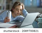 Small photo of Asleep student trying to study with a laptop holding energy drink in the night at home